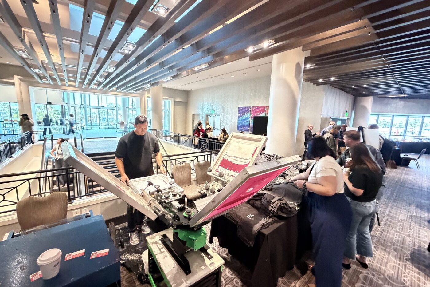 A working live-printing press station set up in a bright venue lobby with guests watching the crew print